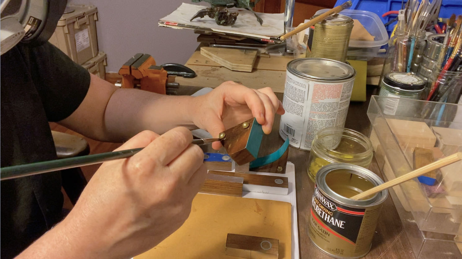 person with respirator sealing wooden blocks with a paintbrush and polyurethane